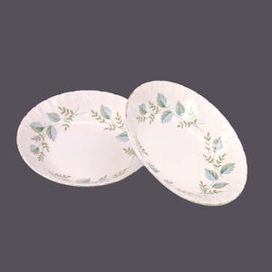 May include: Two white ceramic bowls with a green and blue leaf design. The bowls are slightly scalloped around the edges.