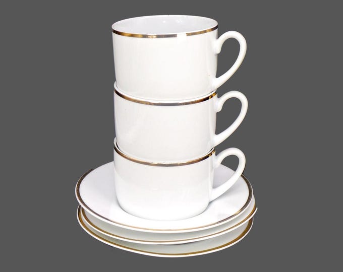Three Skye McGhie white-and-gold coffee cans with matching saucers.