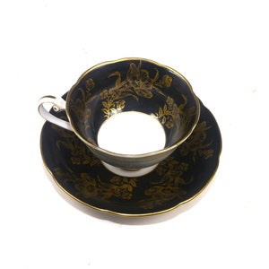 Conjunto de xícara e pires com motivos florais em preto e dourado da Woodville China. Porcelana de ossos feita no Japão. Pequeno defeito (veja abaixo).