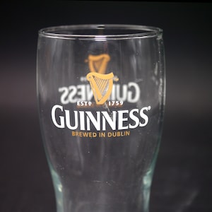 May include: A clear glass pint glass with the Guinness logo and the text "ESTD 1759" and "BREWED IN DUBLIN".