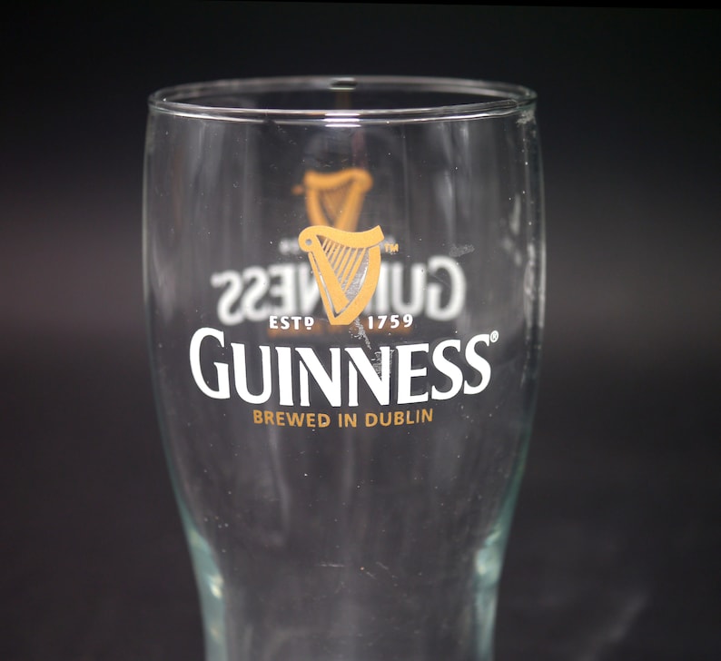 May include: A clear glass pint glass with the Guinness logo and the text "ESTD 1759" and "BREWED IN DUBLIN".