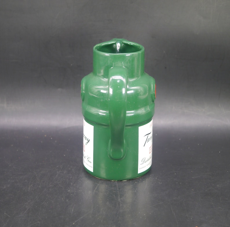 May include: A green ceramic pitcher shaped like a Tanqueray gin bottle. The pitcher has a handle and a label that reads "Tanqueray London Dry Gin."