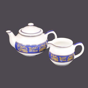 May include: A white teapot and creamer set with blue and gold accents. The teapot and creamer feature the Tetley Teas logo.