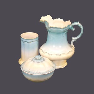 May include: A vintage bathroom set featuring a blue and white jug, a matching soap dish, and a cylindrical tumbler.