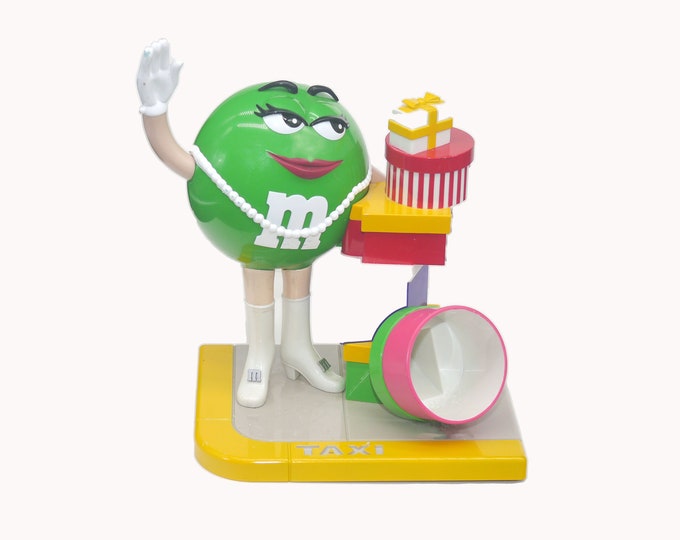 M&M's Candy Dispenser Ms Green Shopper in pearls, iconic go-go boots hailing a taxi after shopping. Missing handbag.