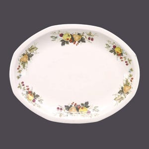 May include: White oval serving platter with a decorative border of green leaves, yellow pears, and red berries.