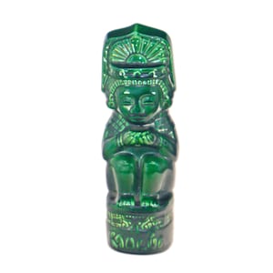 May include: Green ceramic figurine of a person sitting with their hands clasped in their lap. The figurine is wearing a headdress with intricate details and is sitting on a base with a decorative pattern.
