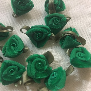 May include: A collection of green fabric rose embellishments with brown ribbon accents. These are perfect for adding a touch of vintage charm to crafts and sewing projects.