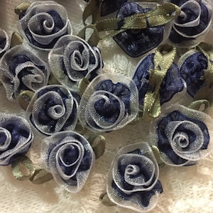 May include: Close-up of navy blue and silver fabric roses with green ribbon accents. These decorative fabric flowers are ideal for crafting projects, scrapbooking, or embellishing clothing and accessories. The roses are approximately 1 inch in diameter.
