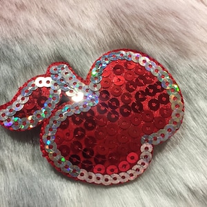 May include: A red heart-shaped sequin patch with a silver border. The sequins are iridescent and create a shimmering effect.
