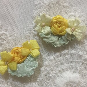 May include: Two handmade fabric flower embellishments in shades of yellow and green. The flowers are made of ribbon and have a delicate, vintage look.