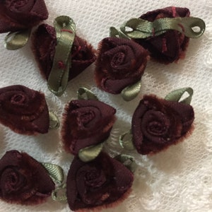 May include: A collection of ten burgundy velvet fabric rose embellishments with green satin leaves. The roses are approximately 1 inch in diameter.