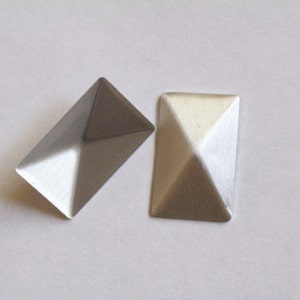 May include: Two silver pyramid-shaped metal studs. The studs are rectangular and have a slightly textured surface.