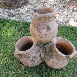 May include: Terracotta planter with three pots, two smaller pots on the sides and a larger pot on top. The pots are all connected and have a rustic, weathered look.
