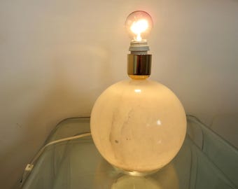 Peut inclure: Une lampe de table en albâtre blanc avec une base dorée et une ampoule transparente. La lampe est posée sur une surface en verre.
