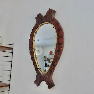 Op de afbeelding: Een houten spiegel met een touwrand en een gesneden visontwerp. De spiegel is ovaalvormig en heeft een donkerbruine afwerking.