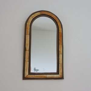 May include: A decorative arched mirror with a brown frame and a cream-colored inlay. The mirror has a simple design and would look great in a modern or minimalist home.