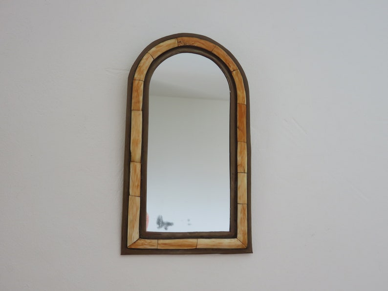 May include: A decorative arched mirror with a brown frame and a cream-colored inlay. The mirror has a simple design and would look great in a modern or minimalist home.