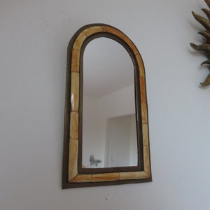 May include: A decorative arched mirror with a brown frame and a light brown and orange patterned border.