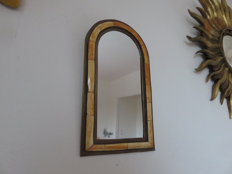 May include: A decorative arched mirror with a brown frame and a light brown and orange patterned border.
