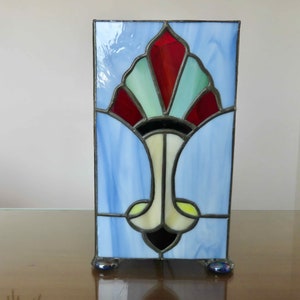 May include: A stained glass panel with a blue background and a stylised floral design in red, green, white, and black.