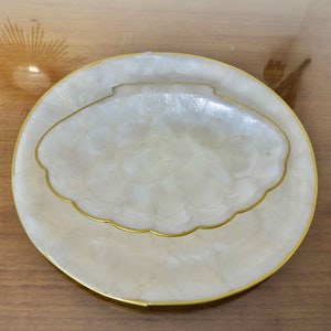 May include: A white, round, decorative plate with a gold rim. The plate has a smaller, white, shell-shaped dish inside with a gold rim.