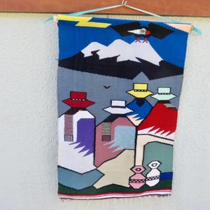 Può includere: Un arazzo rettangolare tessuto raffigurante un paesaggio con una montagna innevata, un'aquila in volo e quattro figure che indossano cappelli. La scena include un fulmine giallo, abiti colorati e due piccoli vasi sul bordo inferiore.