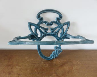 Puede incluir: Estantería de pared adornada de color turquesa, con un diseño decorativo de inspiración Art Nouveau. La estantería presenta un diseño calado curvado con un anillo central y una balda inferior. La pieza es de metal y tiene un acabado envejecido.