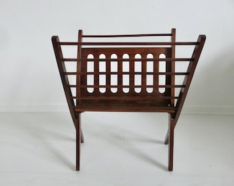Puede incluir: Un revistero de madera marrón oscuro con un patrón de rejilla. El revistero tiene un diseño sencillo con una base rectangular y patas inclinadas.