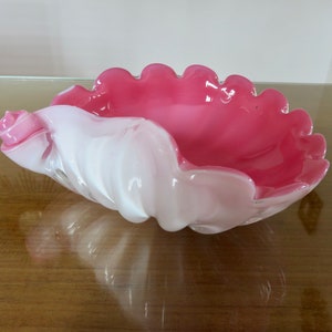 May include: A pink and white glass shell-shaped dish with a ruffled edge. The dish is made of glass and has a glossy finish.