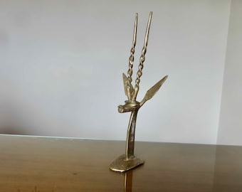 Puede incluir: Una escultura de metal dorado de una cabeza de antílope con cuernos retorcidos. La escultura está sobre una pequeña base y mide unos 25 cm de alto.