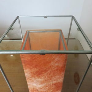 May include: A contemporary lamp with a clear glass top and a metal frame. The interior has an orange, textured shade. The lamp's design is minimalist and suitable for various interior styles. The measurements are in centimetres.