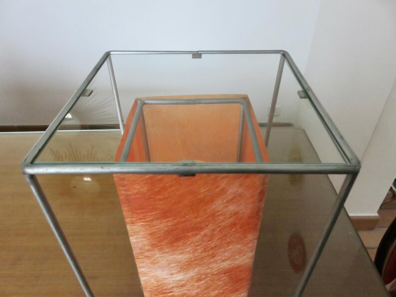 May include: A contemporary lamp with a clear glass top and a metal frame. The interior has an orange, textured shade. The lamp's design is minimalist and suitable for various interior styles. The measurements are in centimetres.