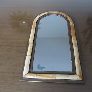 May include: A decorative mirror with a light brown frame made of bone-like material. The mirror has an arched top and a rectangular shape.