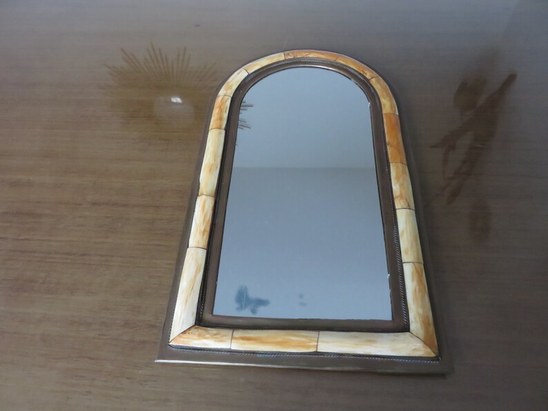May include: A decorative mirror with a light brown frame made of bone-like material. The mirror has an arched top and a rectangular shape.
