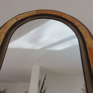 May include: A large, arched mirror with a decorative frame made of beige and brown tiles. The frame has a rope-like design around the edge.