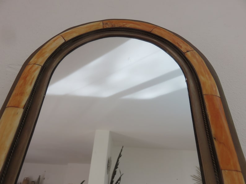May include: A large, arched mirror with a decorative frame made of beige and brown tiles. The frame has a rope-like design around the edge.