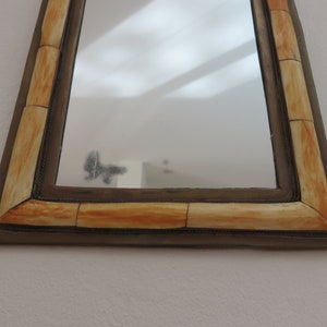 May include: A rectangular mirror with a decorative frame made of ivory-colored bone. The frame has a dark brown border.