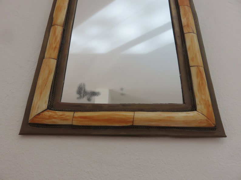 May include: A rectangular mirror with a decorative frame made of ivory-colored bone. The frame has a dark brown border.