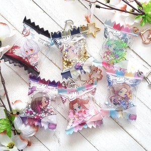 May include: Six colourful, clear plastic keychain charms with glitter inside. Each charm features a different anime character with a speech bubble that says "POMS!"