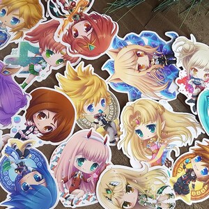 Peut inclure: Une collection d'autocollants color&eacute;s de style anime, repr&eacute;sentant divers personnages aux grands yeux et aux cheveux d&eacute;taill&eacute;s. Les autocollants pr&eacute;sentent une vari&eacute;t&eacute; de poses et de tenues, certains sur des fonds d&eacute;coratifs. Les autocollants sont sur une surface brune.