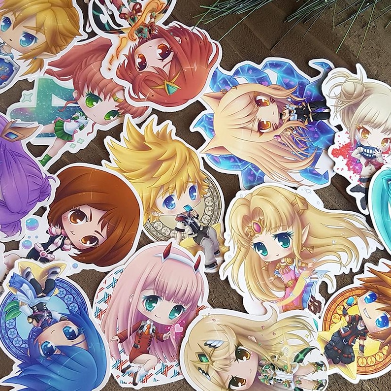 Peut inclure: Une collection d'autocollants color&eacute;s de style anime, repr&eacute;sentant divers personnages aux grands yeux et aux cheveux d&eacute;taill&eacute;s. Les autocollants pr&eacute;sentent une vari&eacute;t&eacute; de poses et de tenues, certains sur des fonds d&eacute;coratifs. Les autocollants sont sur une surface brune.