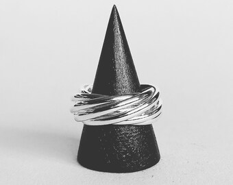 May include: A silver ring with a twisted design, displayed on a black cone-shaped ring holder.