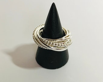 May include: A silver ring with a beaded design. The ring is made of multiple bands that are intertwined. The ring is displayed on a black cone-shaped stand.