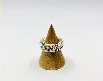May include: A silver ring made of multiple thin bands stacked on top of each other. The ring is displayed on a wooden ring holder.