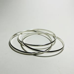 Könnte beinhalten: Drei silberne Armreifen, die übereinander gestapelt sind. Die Armreifen sind alle glatt und glänzend.