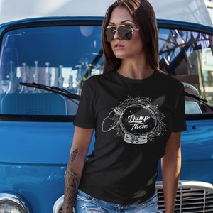 Könnte beinhalten: Schwarzes T-Shirt mit weißer Grafik einer Kristallkugel und dem Schriftzug "Dump Them". Das Design ist von Strahlen und Sternen umgeben. Das kurzärmelige Shirt ist aus weichem Material.