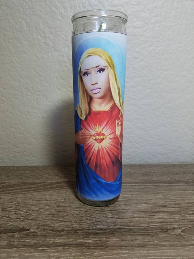 May include: A glass candle with a colorful image of a woman with a crown of thorns and a red heart with flames. The woman is wearing a blue robe.