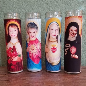 May include: Four glass candle holders with colorful images of women. Each candle holder features a woman with a heart and a halo. The candles are a fun and unique way to add a touch of humor to your home decor.