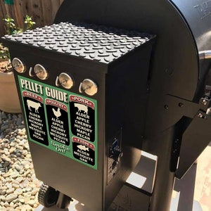 May include: A black smoker grill with a green and red sticker that says "Pellet Guide" and lists different wood types for smoking beef, poultry, pork, and fish. The sticker includes the text "Smoke On!"